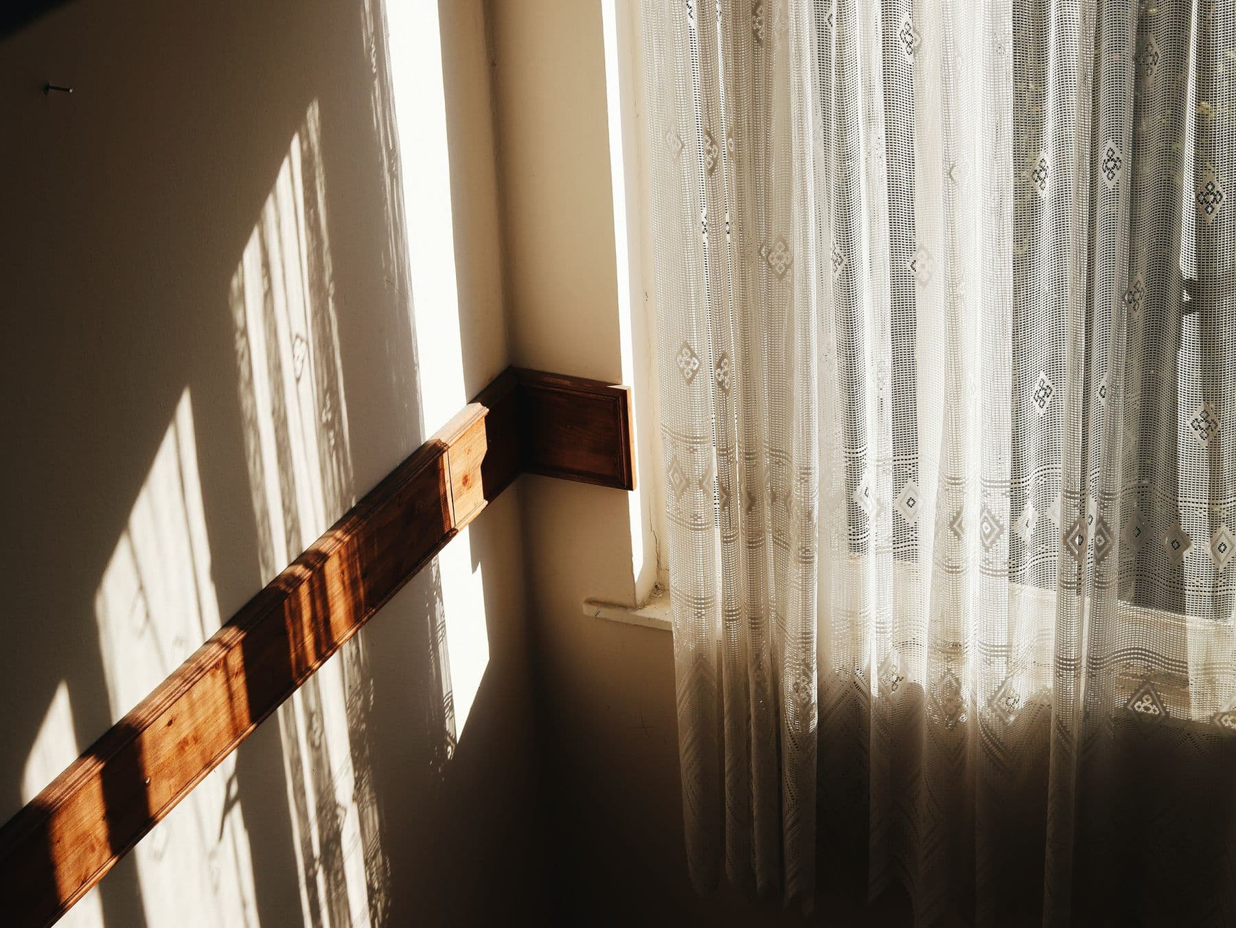 Late afternoon light falling through a lace curtain onto a plain wall