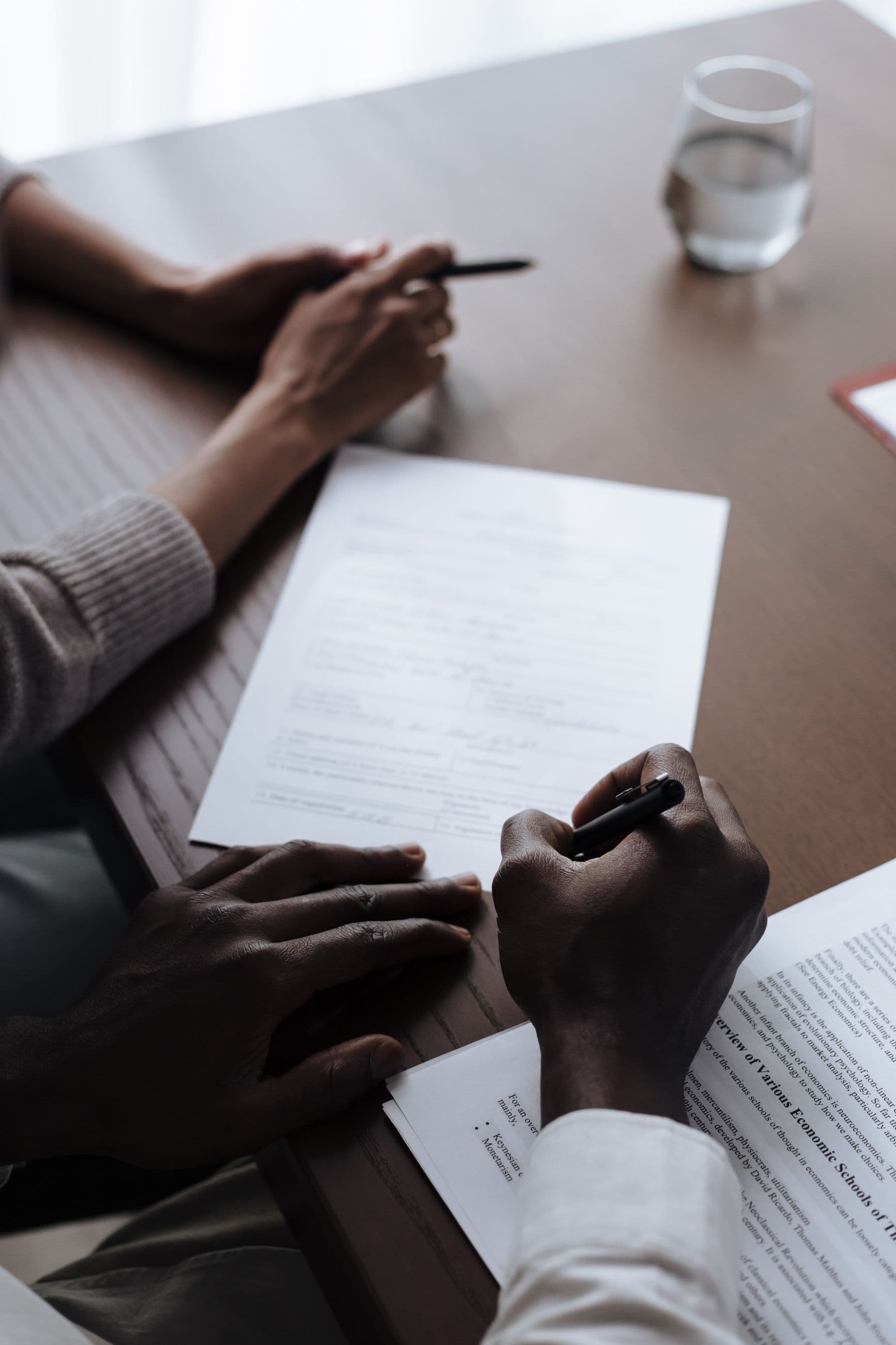 Two pairs of hands at a wooden table with a printed form and pens