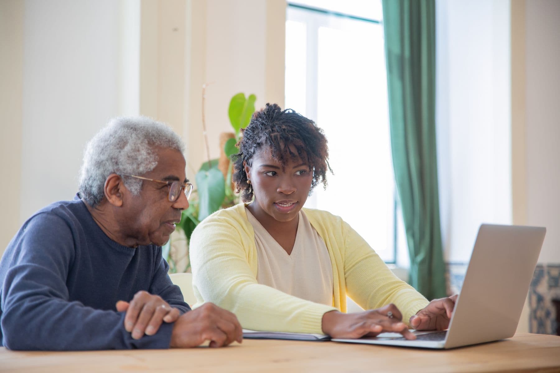 An older man and a younger woman at a kitchen table, looking at a laptop together